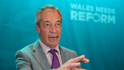 Nigel Farage with Reform UK branded backdrop behind him