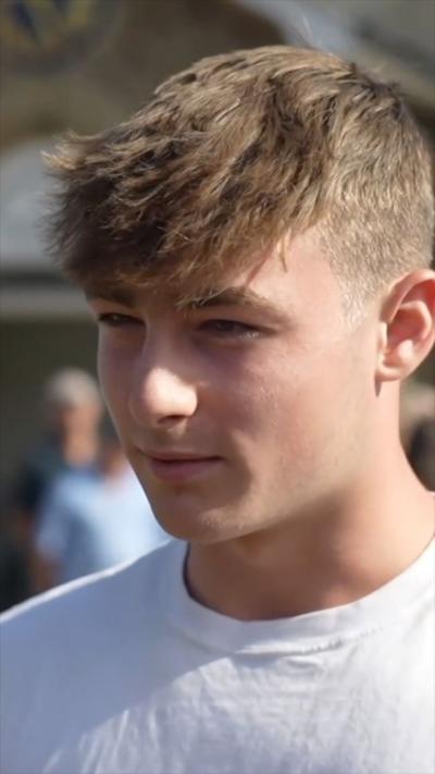A teenager wears a white tshirt speaking with blonde short hair.