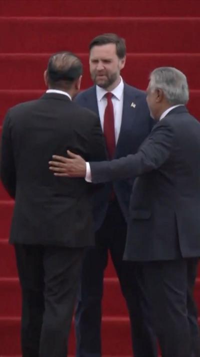 US Vice President JD Vance standing in front of three people, with an red-carpeted airstair behind him.