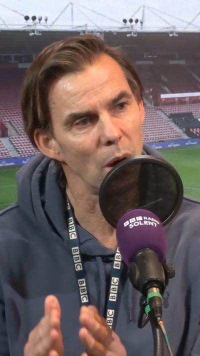 Man in a hoodie speaks into a microphone.