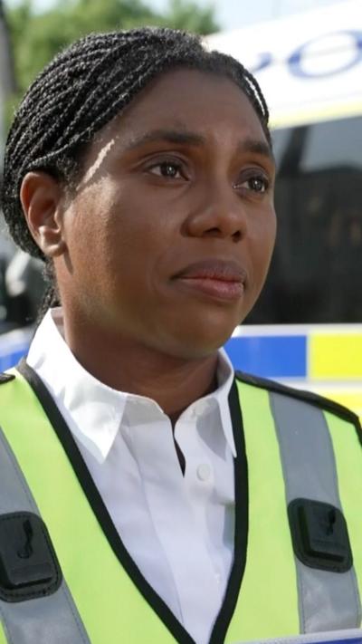 Kemi Badenoch wearing white shirt and yellow vest during interview