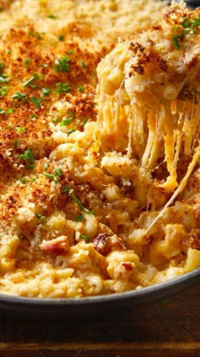 Close up view of mac and cheese. A forkful is being lifted from the dish with lots of stringy melty cheese