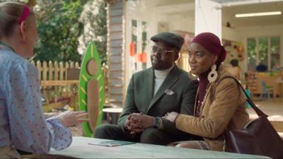 Funmi and Maurice sit together in the garden of a nursery, talking to a staff member