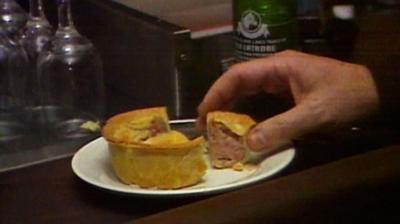 A hand picking up a piece of pork pie in a bar in New York.