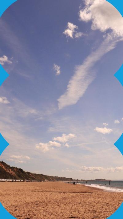 Beach with sea in distance and blue sky with white wispy clouds.