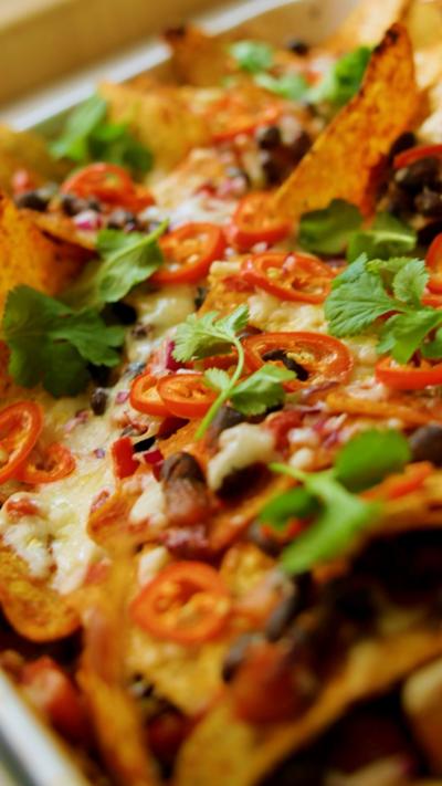 A close up of baked nachos topped with cheese, chilli slices and coriander
