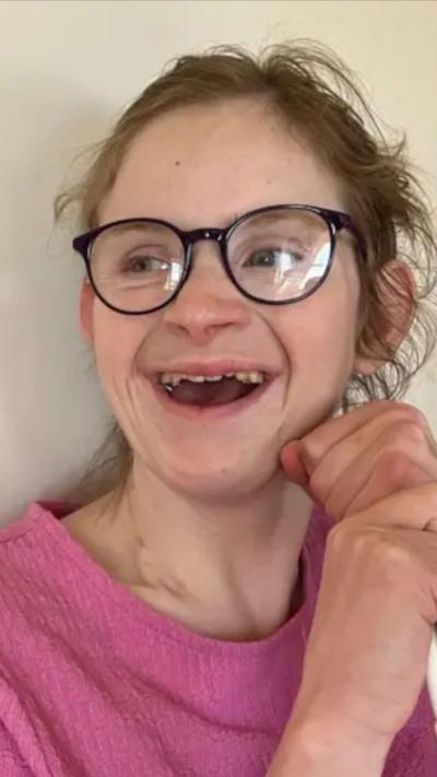 A young woman wearing glasses and smiling. She is wearing a pink t-shirt