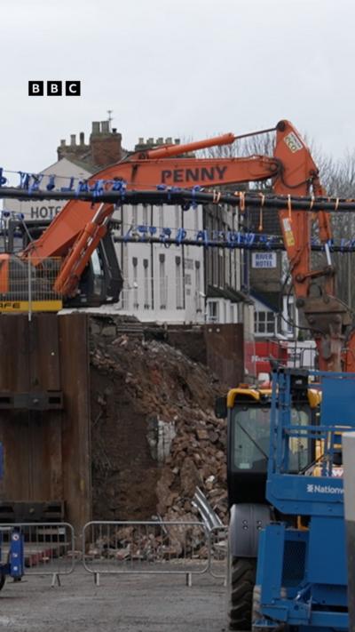 A red crane in the background with a blue vehicle in the forground.
