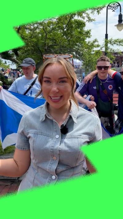 Presenter smiling at camera with Scotland flags behind her