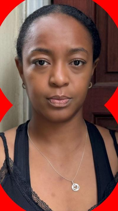 A woman with dark hair pulled back from her face stands in front of a door wearing a silver necklace