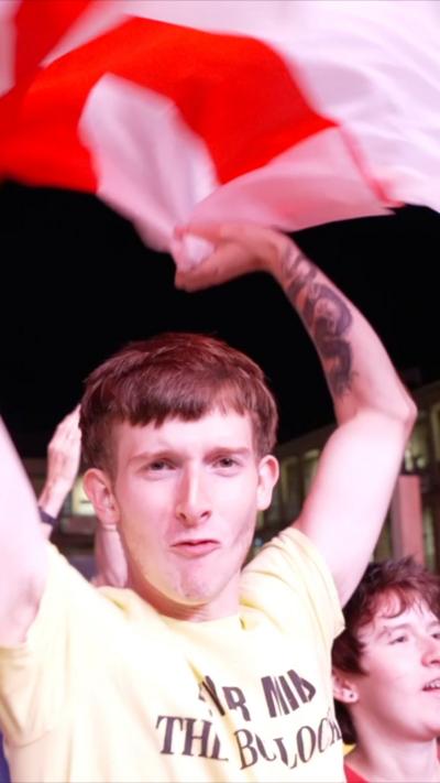A man in a yellow t-shirt holds an red and white England flag aloft