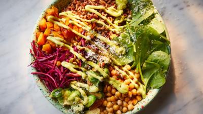 A bowl filled with  roast pumpkin, crispy chickpeas, charred sprouts, zesty red cabbage and a creamy avocado sauce.