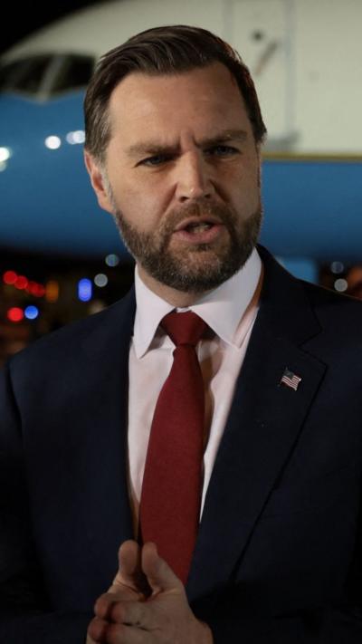 Vice-president JD Vance speaks to reporters in front of Air Force Two, as he wears a blue suit and red tie.