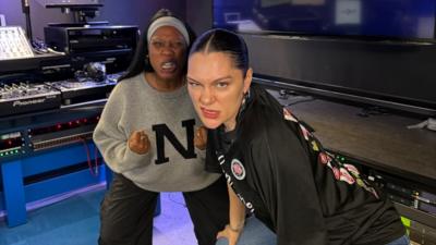 Jessie J and Nadia Jae make faces while crouching in a radio studio