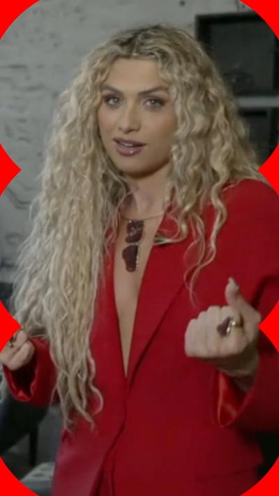 Antigoni Buxton stands and looks at the camera. She wears a red blazer and bunches her fits.