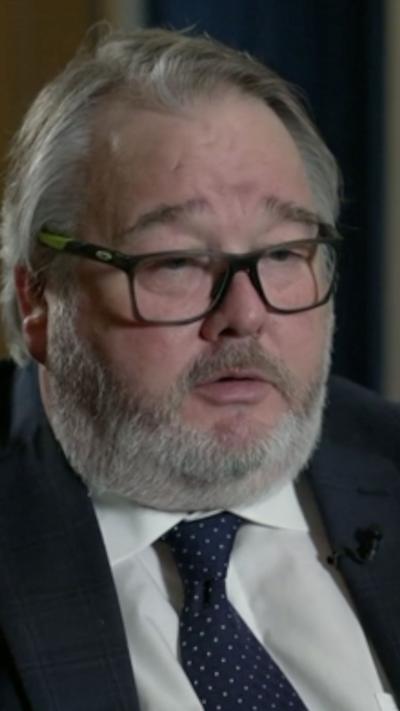 A man with white hair and a beard and glasses, wearing a blue tie