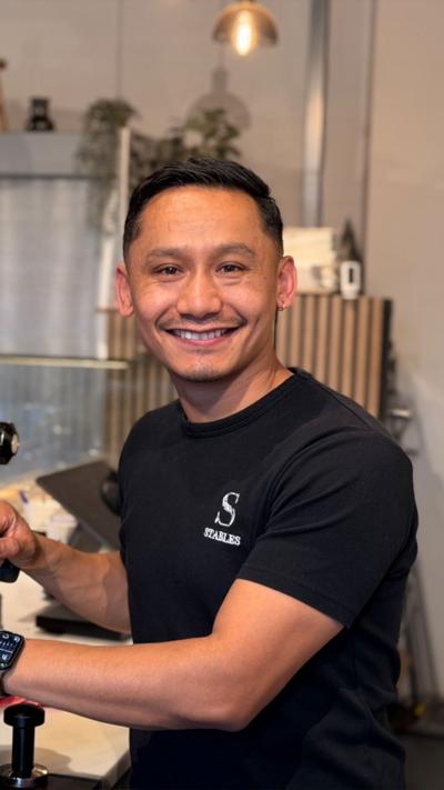 Shyam Lama weaing a black tshirt. He is smiling and standing in a cafe.