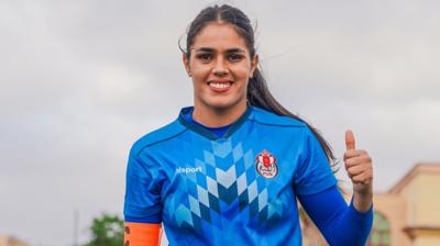 Kawtar Bentaleb, wearing a blue goalkeeper's jersey, gives a thumbs up gesture with her left hand