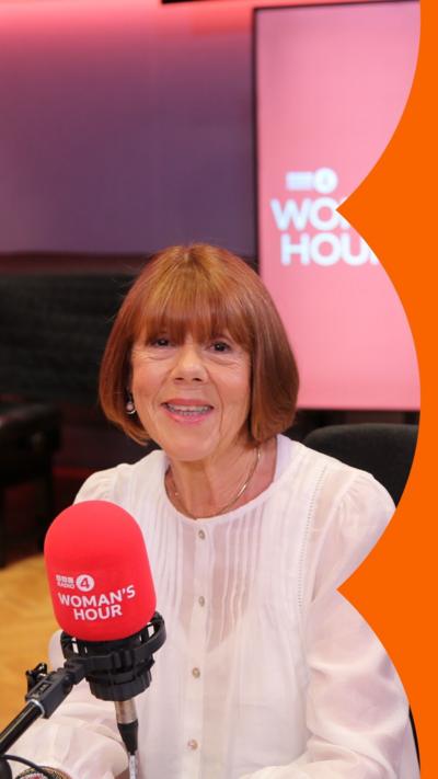 Gisèle Pelicot wears a white blouse and sits behind a microphone. She smiles at the camera.