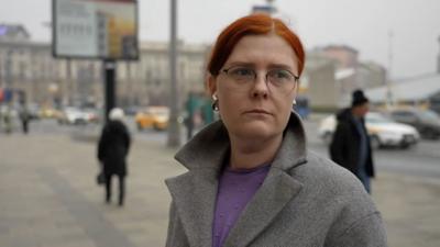 A Russian woman with red hair speaks to reporters