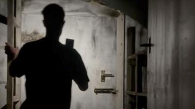 A silhouetted man standing in front of a bolted door 