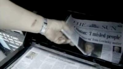 A hand lifts a copy of The Sun Newspaper. An article about Clinton and the Lewinsky affair is on the front pagethe 