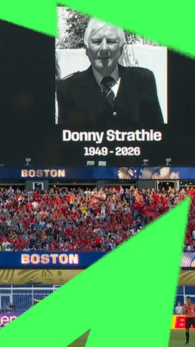 A black and white photo of Donny Strathie with 1949-2026 is on the screen above a packed football pitch.