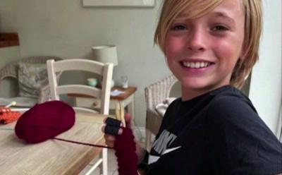 boy holding knitting yarn sits at table smiling