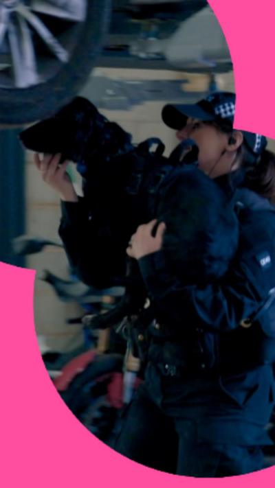 A black dog being carried by a female police officer under an elevated car