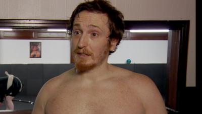 A man looking to the left of the camera, he has dark hair and a beard.