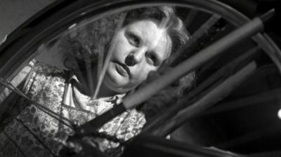 The face of a young woman through the spokes of a bicycle wheel as she paints it with grease.