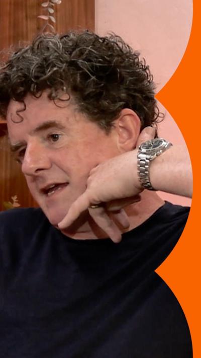 A man with short, dark curly hair mimes holding a phone to his ear
