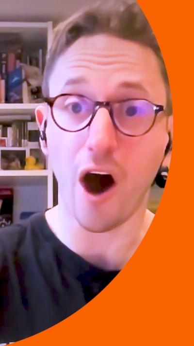 A man in a black T-shirt and glasses looks at the camera with his mouth open in surprise