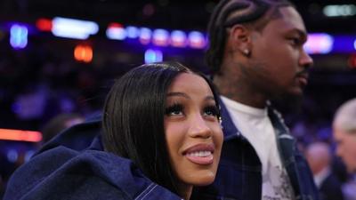Rapper Cardi B with her boyfriend Stefon Diggs who has his arm around her. Stefon is on the right and in the background looking ahead while Cardi B is in the centre of the picture looking towards the sky