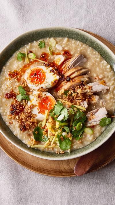 Top down view of a green bowl with chicken congee in. It sits on a wooden plate.
