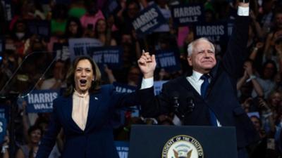 Kamala Harris and Tim Walz hold arms up at rally