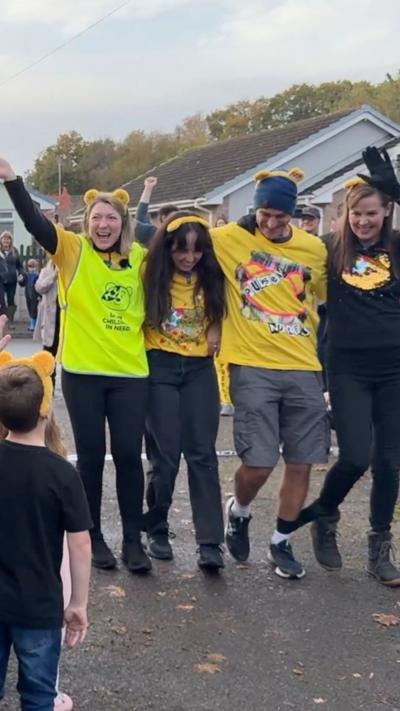 A group of four people with their arms around each other and smiling complete their challenge. They have black elastic straps around their ankles and wear yellow Children in Need t shirts.