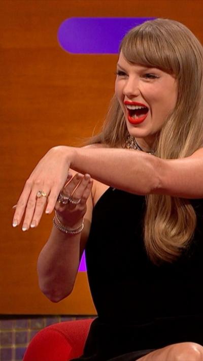 Taylor Swift smiles while holding out her left hand to show her engagement ring