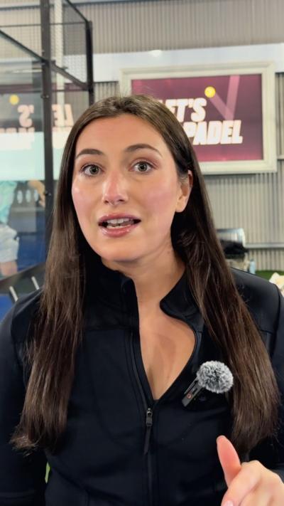 A woman with dark hair and a black top standing in front of a sign that says Let's Padel