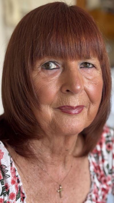 A woman with a red/brown bob wearing a white top with red and green flowers on it