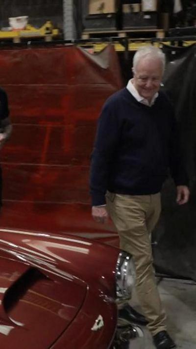 BBC Points West Presenter David Garmston walks near the bonnet of a red 1961 Aston Martin