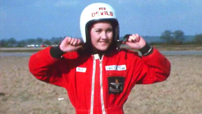 Jackie Smith wearing a Red Devils parachute uniform taking off her helmet.