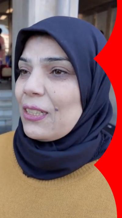 A woman wearing a yellow top and a blue headscarf, speaking to the camera