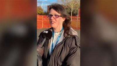 A young woman with brown hair, bleached eyebrows and glasses, speaks to the BBC