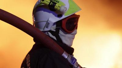 Firefighter holding a hose in front of a fire.