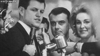 One of the Kennedy brothers stands in front of a microphone