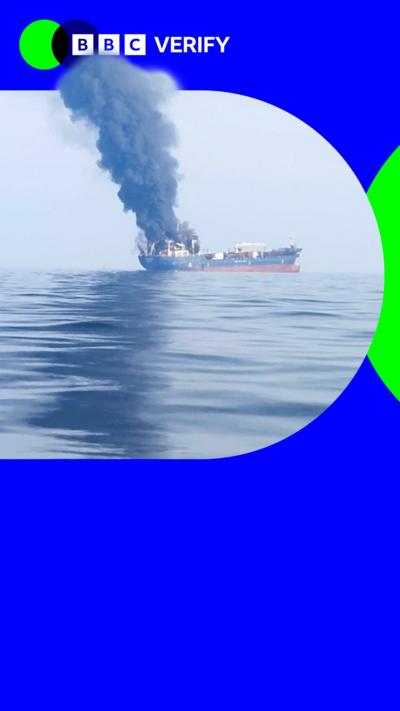 A ship is seen at sea with smoke billowing from it. The photo is imposed over the BBC Verify colours and branding. 