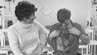 John Noakes shows off the fake hairy chest on himself while Valerie Singleton looks on.