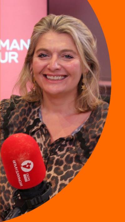 Bryony Gordon wearing a leopard print shirt with a large collar. She's smiling, and sitting in front of a red mic.