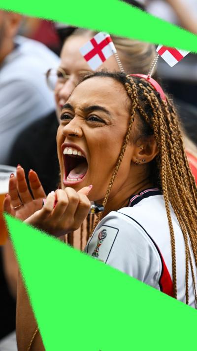A young woman in a beer garden, wearing an England shirt and flags on hear headband, screaming at the TV screen